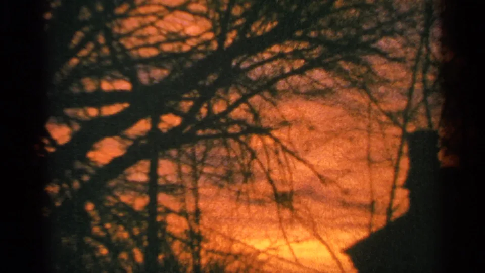 1964 Milwaukee home-movie frame showing silhouetted limbs and a dark roofline or structure edge against orange dusk light.