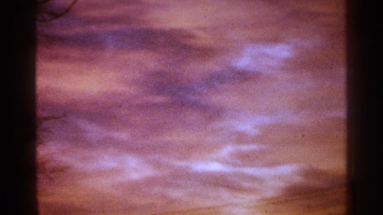 Pink and purple clouds seen through dark vertical film edges.