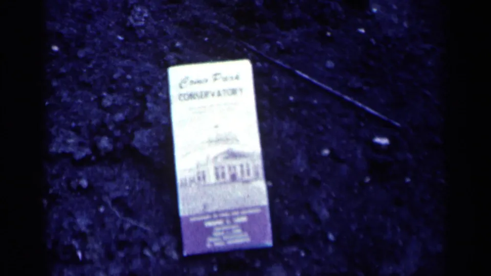 The brochure remains on dark pavement in a soft, blue-tinted 1964 home-movie view from Minnesota.