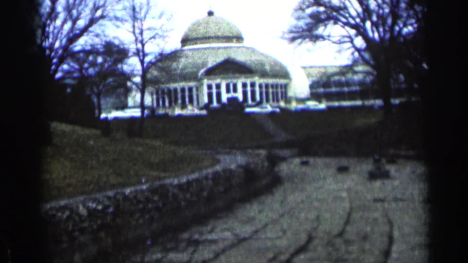 1964 Minnesota 8mm frame of a domed building and columned entrance, partly framed by bare trees.