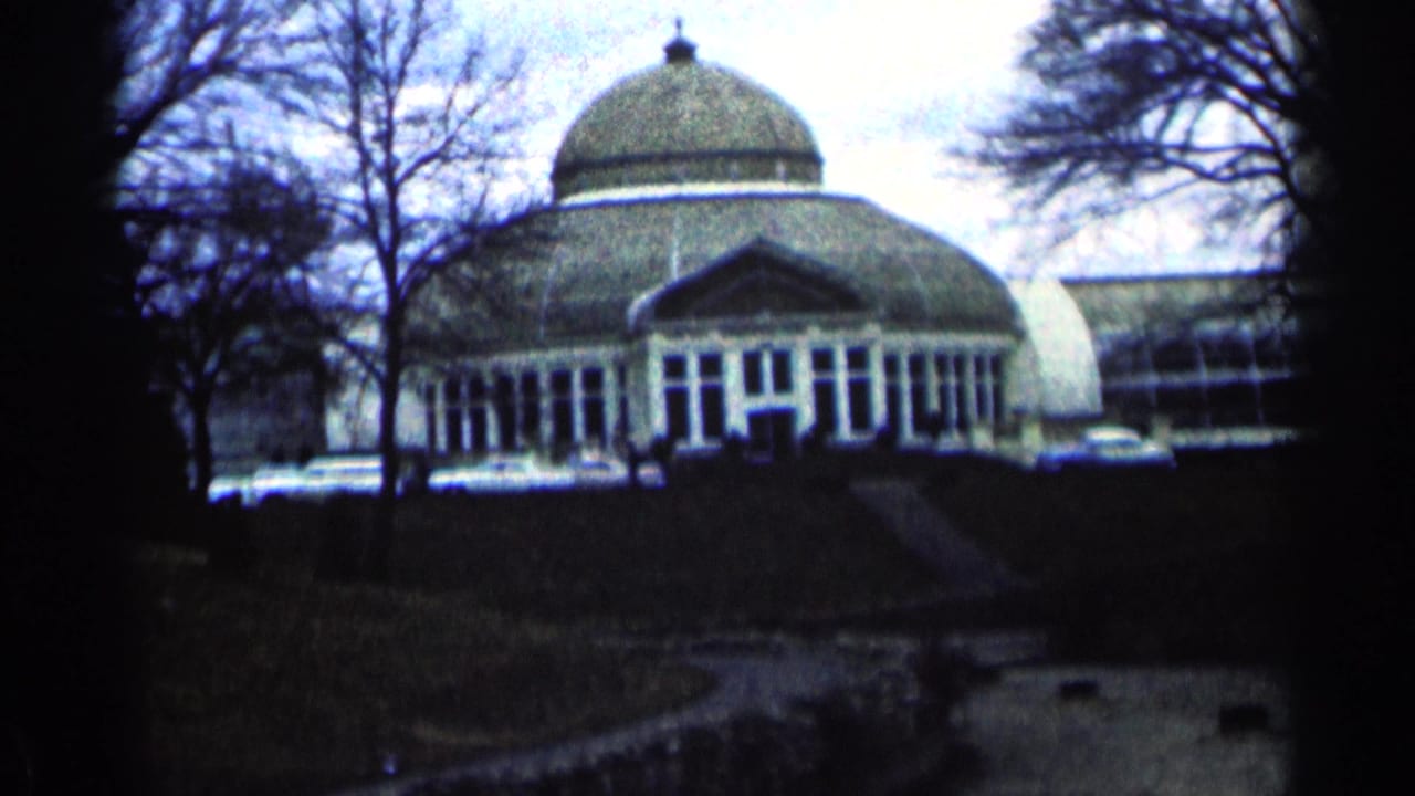 Domed building with glass front, bare trees, lawn, and a path leading toward the entrance.