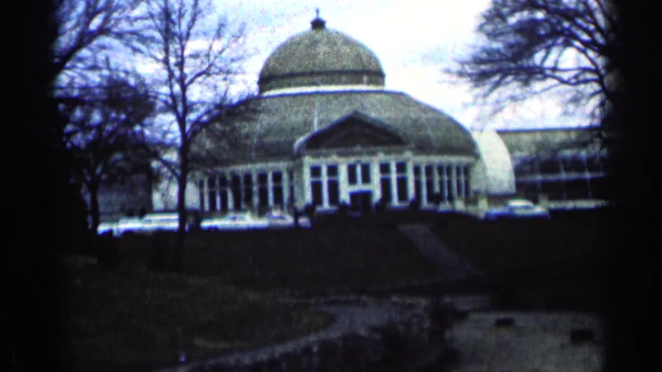 1964 Minnesota home-movie frame showing the domed building from a wide visitor viewpoint, with trees and a walkway in front.