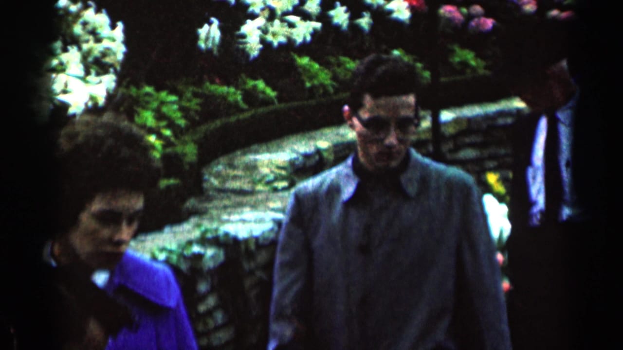 Adults walking past flower beds and stone edging in a dark garden scene.