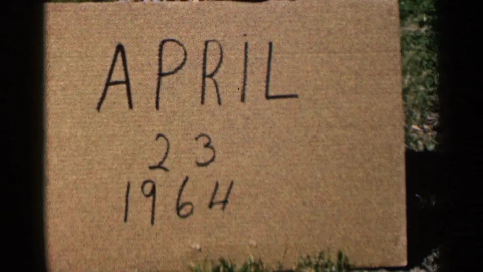 Handwritten cardboard date card reading April 23, 1964, filmed outdoors on grass in the 8mm home movie.