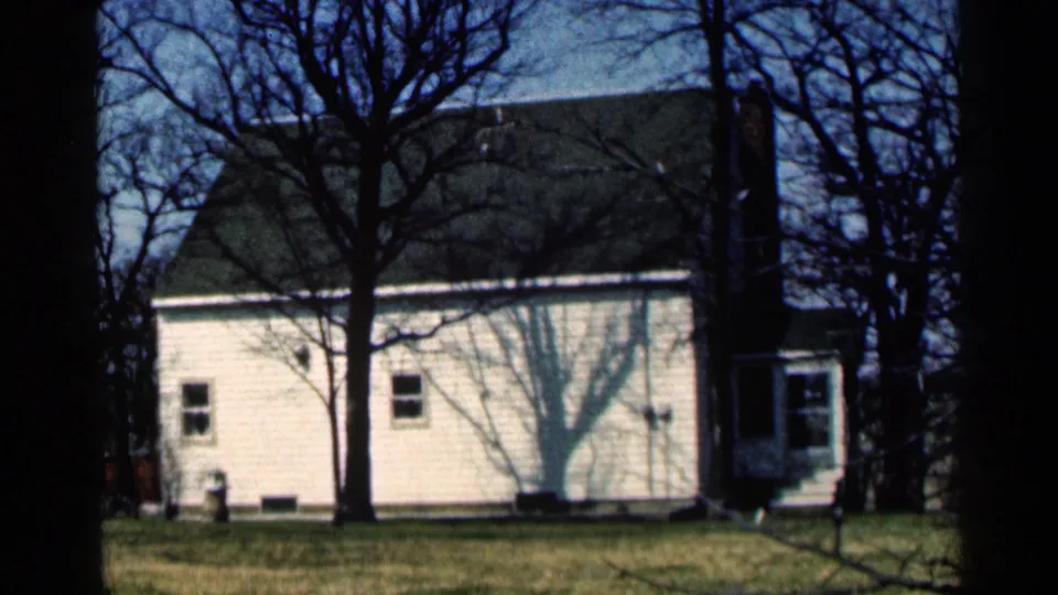 1964 Minnesota frame showing the side elevation of a white clapboard house, lawn, bare trees, windows, and roofline.