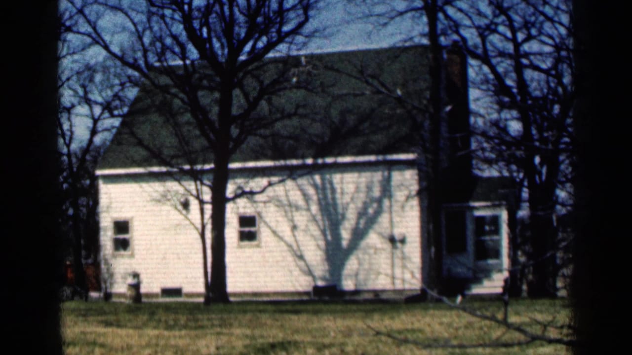 White clapboard house behind bare trees with lawn in front.