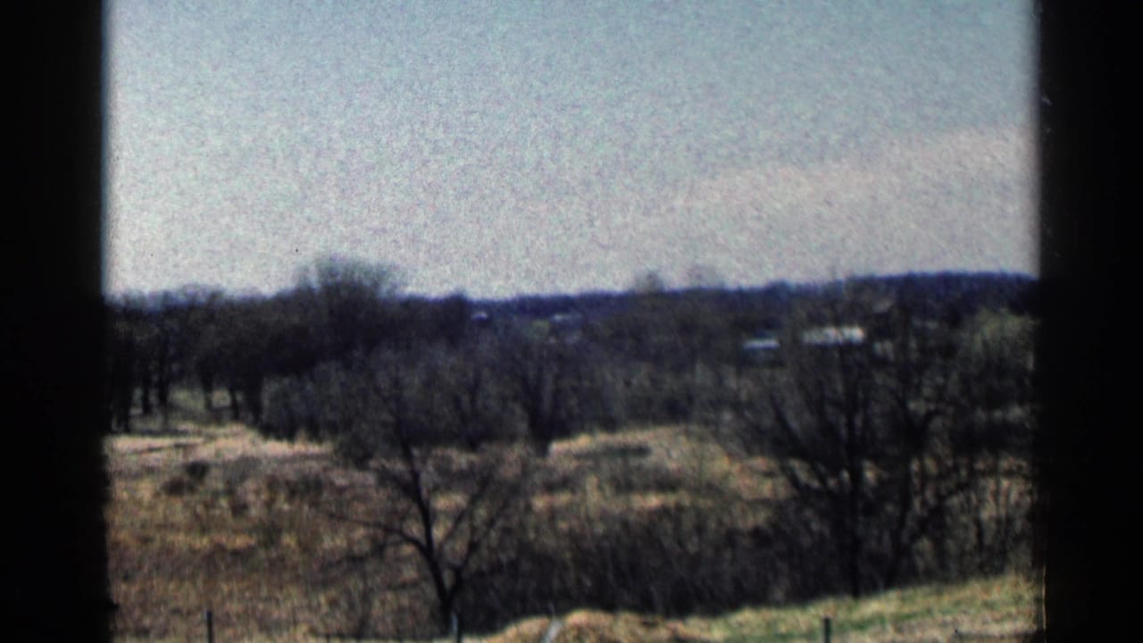 Rural field with leafless trees and distant buildings seen through dark frame edges.