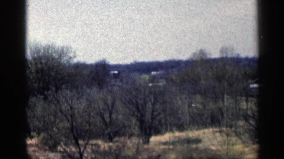 1964 Minnesota home-movie frame with bare trees, distant open land, small far-off structures, and dark 8mm frame edges.