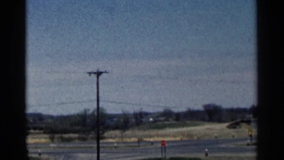 A rural Minnesota road scene includes a utility pole, overhead wires, open fields, and roadside signs in faded 8mm color.