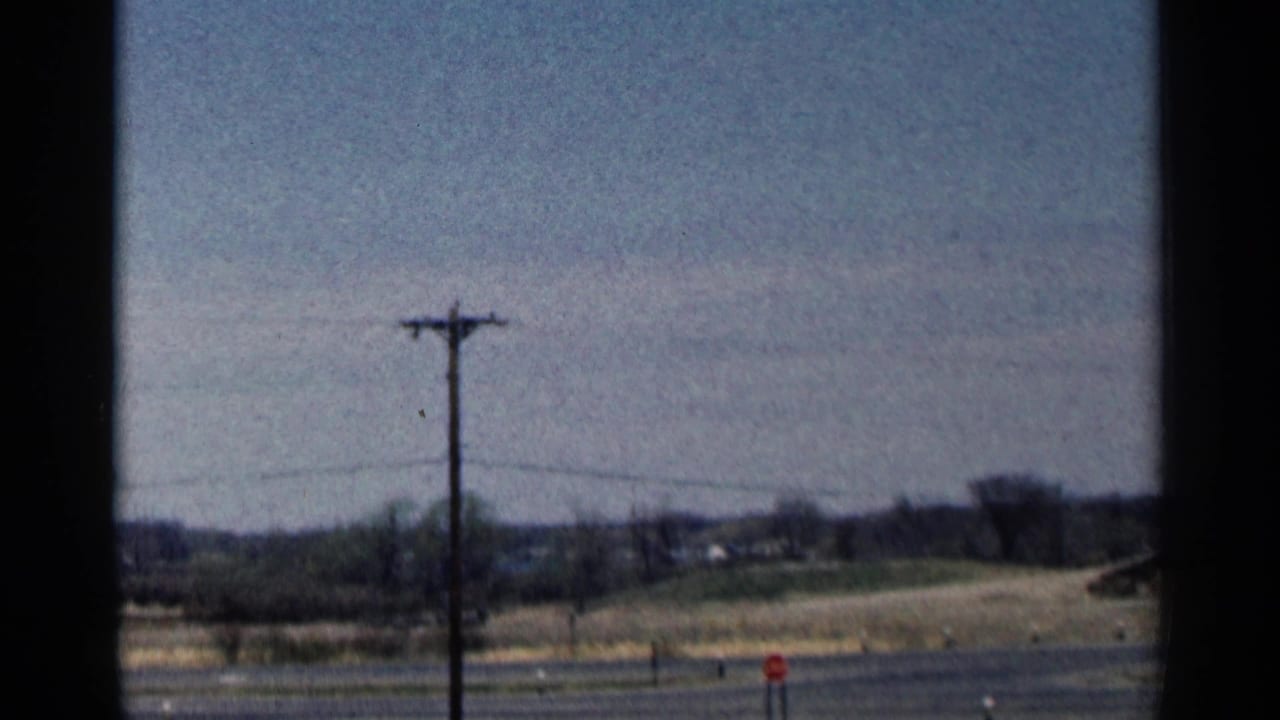 Wooden telephone pole beside a rural road with fields and distant trees.