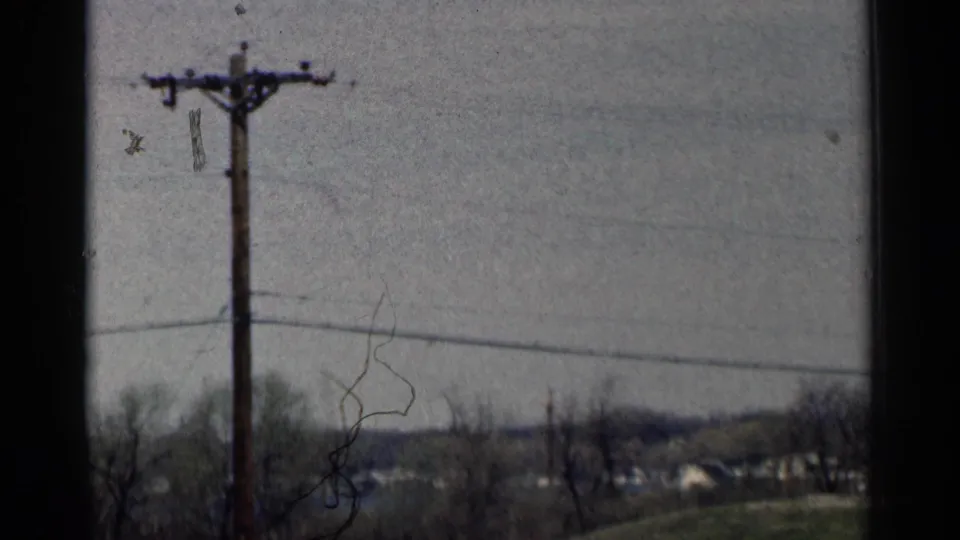 1964 Minnesota 8mm frame showing a utility pole, wire, bare trees, and distant houses under an overcast sky.