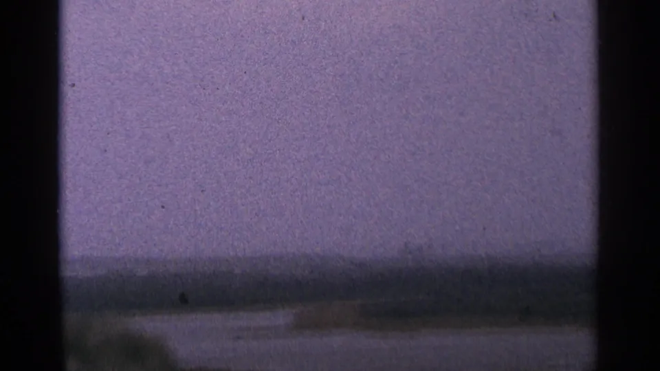 1964 Minnesota 8mm frame showing a blurred lakeside or river view with low shore, overcast sky, and visible film gate edges.