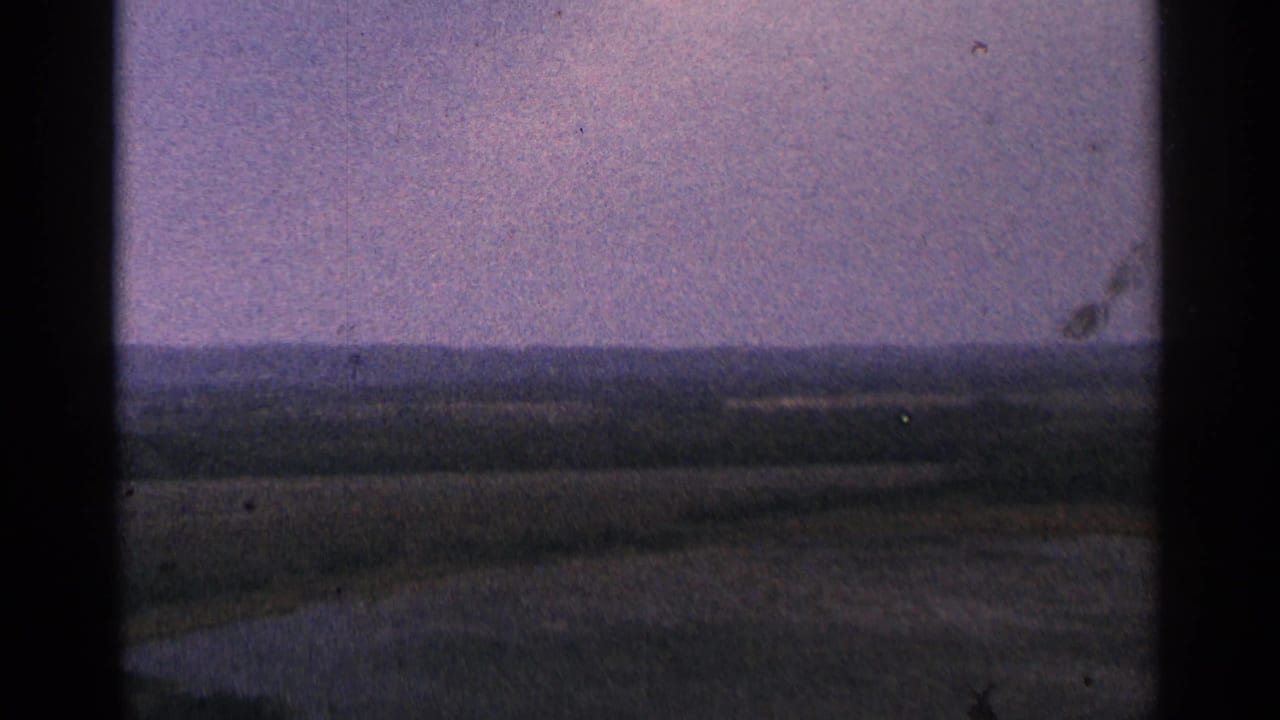 Distant low hills beyond open fields under a purple-tinged sky.
