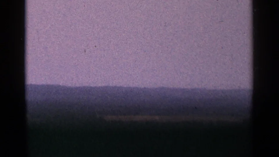 1964 Minnesota 8mm frame showing a purple-toned horizon or sky above a dark band, with heavy grain and film-edge darkness.