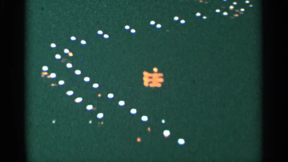 1964 Minnesota 8mm night frame with white points of light spread diagonally across a green-black field and a small orange illuminated shape.