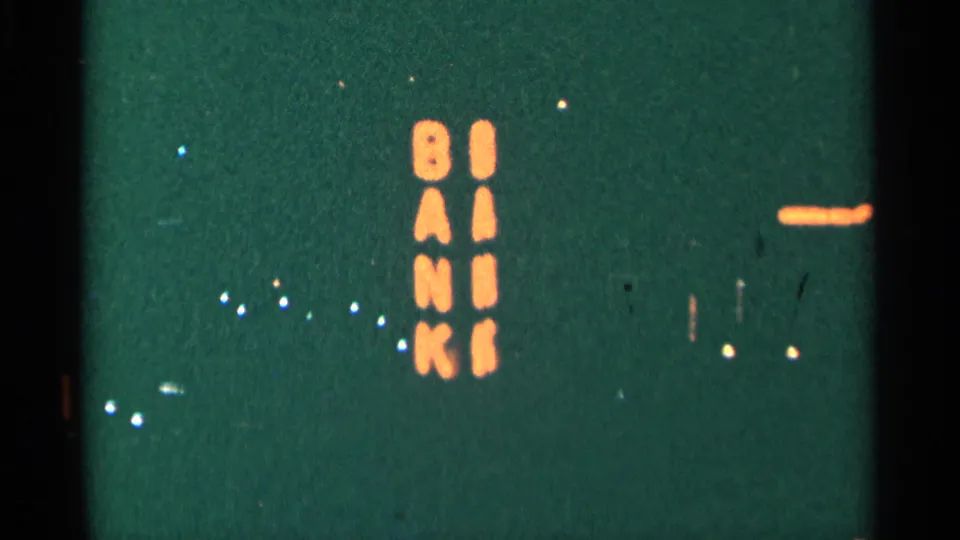 Minnesota 1964 8mm night view with orange vertical letters spelling BANK and scattered small lights nearby.