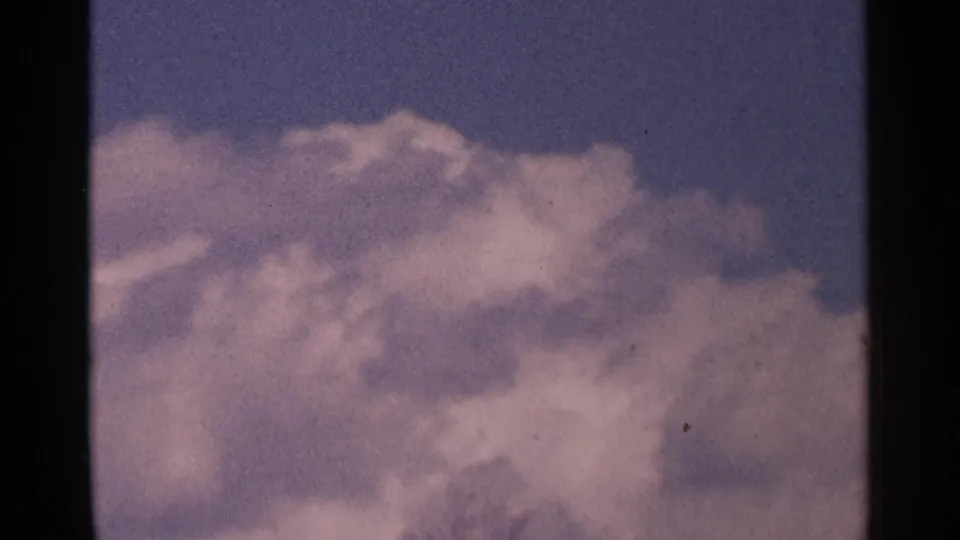 Vintage 8mm frame from Minnesota in 1964 showing a broad cloud mass against a blue-purple sky during a handheld upward view.