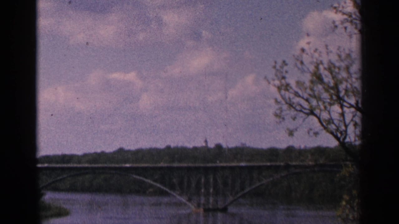 Distant arched bridge crossing a river with trees and cloudy sky.