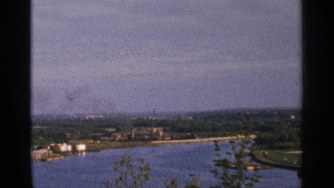 Wide river bend with distant buildings, shoreline, trees, and dark frame edges.