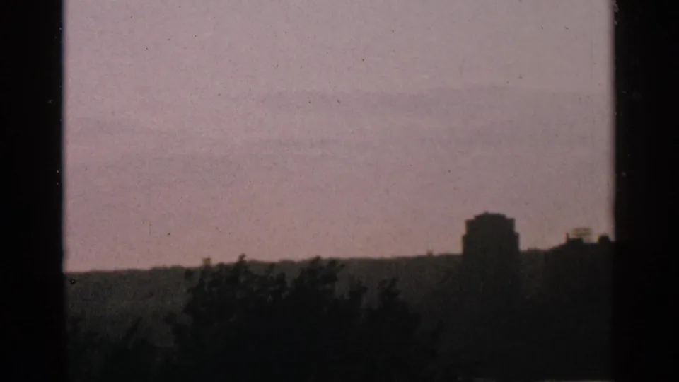 1964 Minnesota 8mm frame with dark trees and building silhouettes against a softly colored dusk sky.