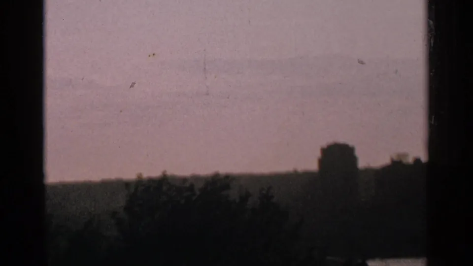 1964 Minnesota 8mm frame showing a hazy dusk or dawn lake horizon with trees and a distant building in silhouette.