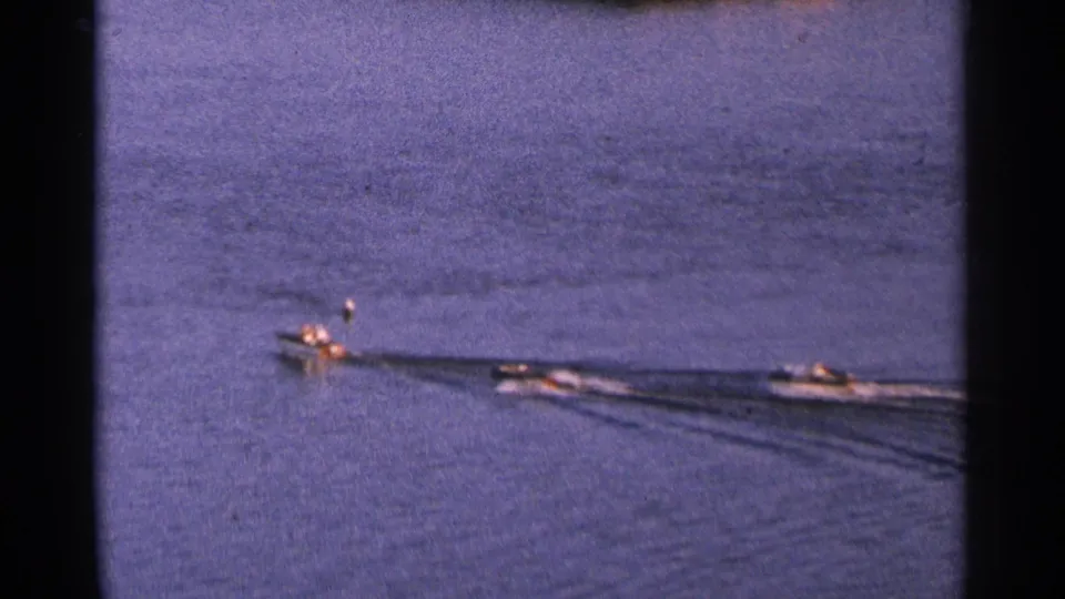 1964 Minnesota home-movie frame of small motorboats gliding across open water with soft focus and visible film grain.