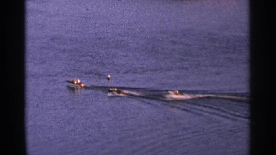 Blue-toned 8mm frame from 1964 Minnesota showing several small motorboats moving across a calm lake with visible wakes.