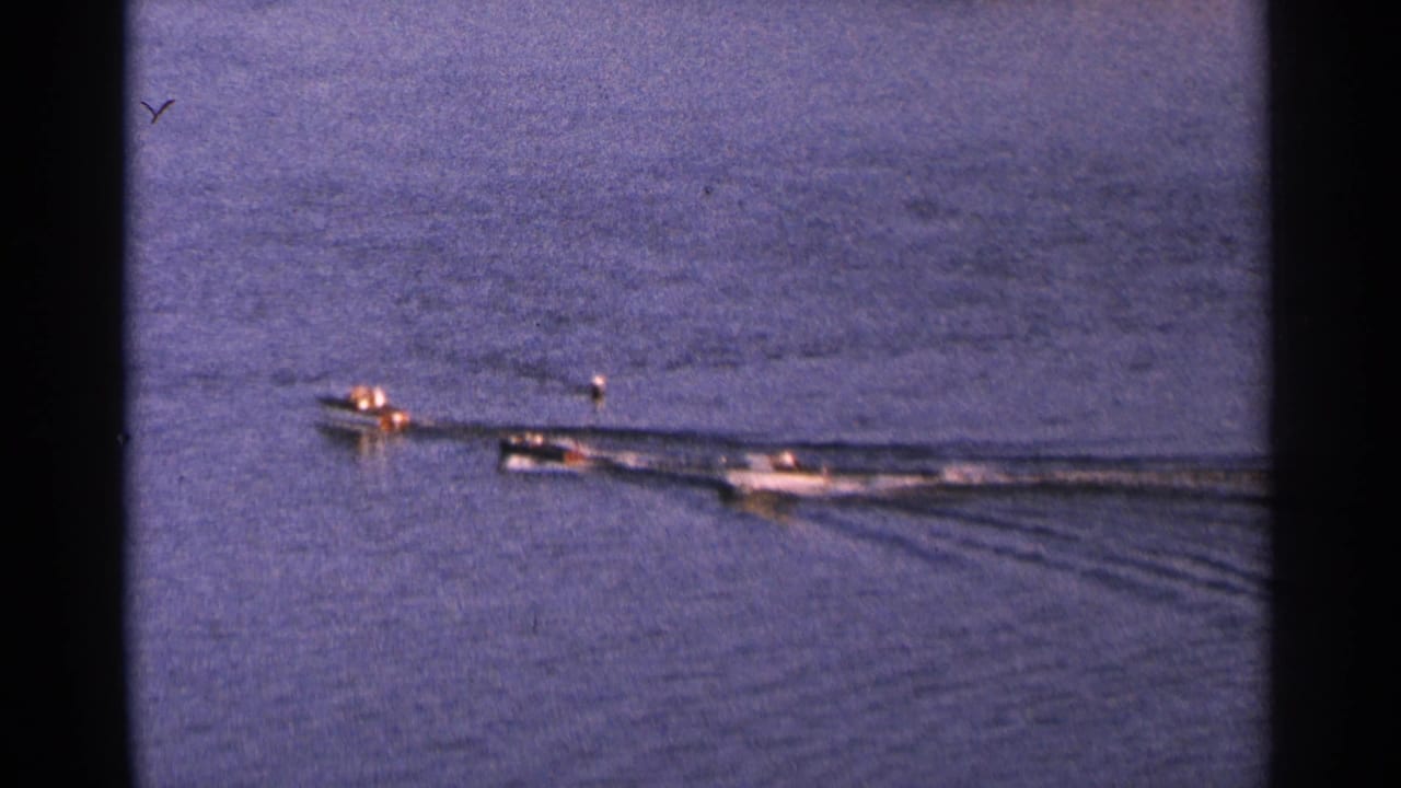 Three small motorboats cross calm lake water, leaving long white wakes behind them.