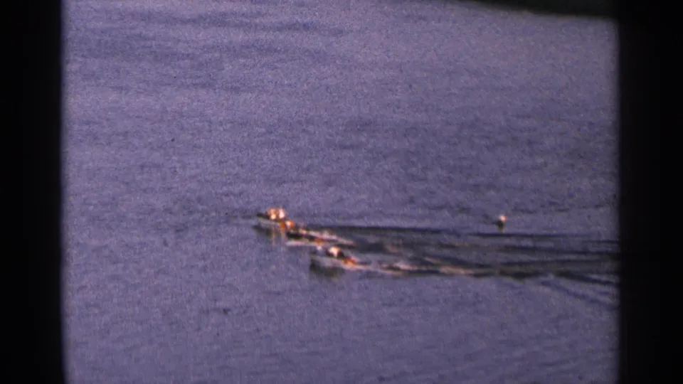 Three small racing boats pass through the frame on a Minnesota lake, captured in soft, grainy 1964 home-movie footage.