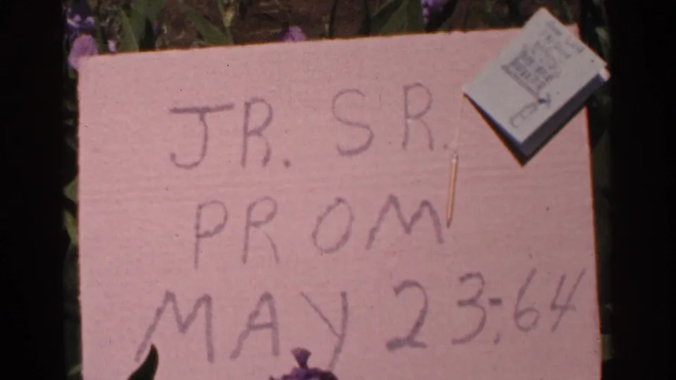 The handmade junior-senior prom sign is shown more fully against greenery, with a small card pinned at the top right.