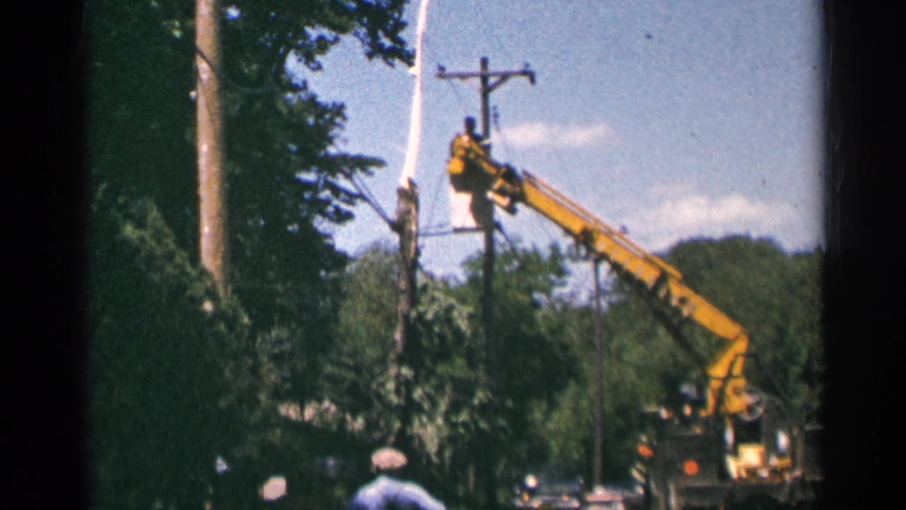 Yellow bucket truck beside a wooden utility pole with a worker elevated near overhead wires.
