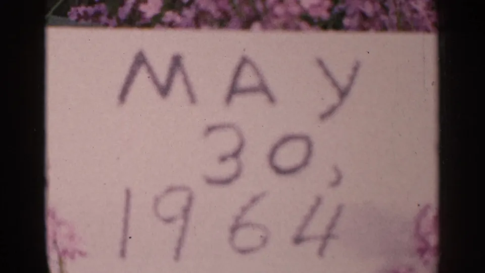Another 8mm frame of the handwritten May 30, 1964 card, with purple floral edges and visible film grain.