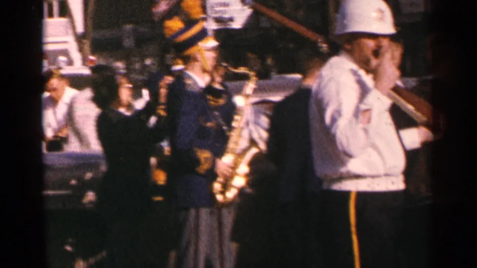 1964 Minnesota parade scene with uniformed band members holding saxophones or brass instruments as spectators watch nearby.