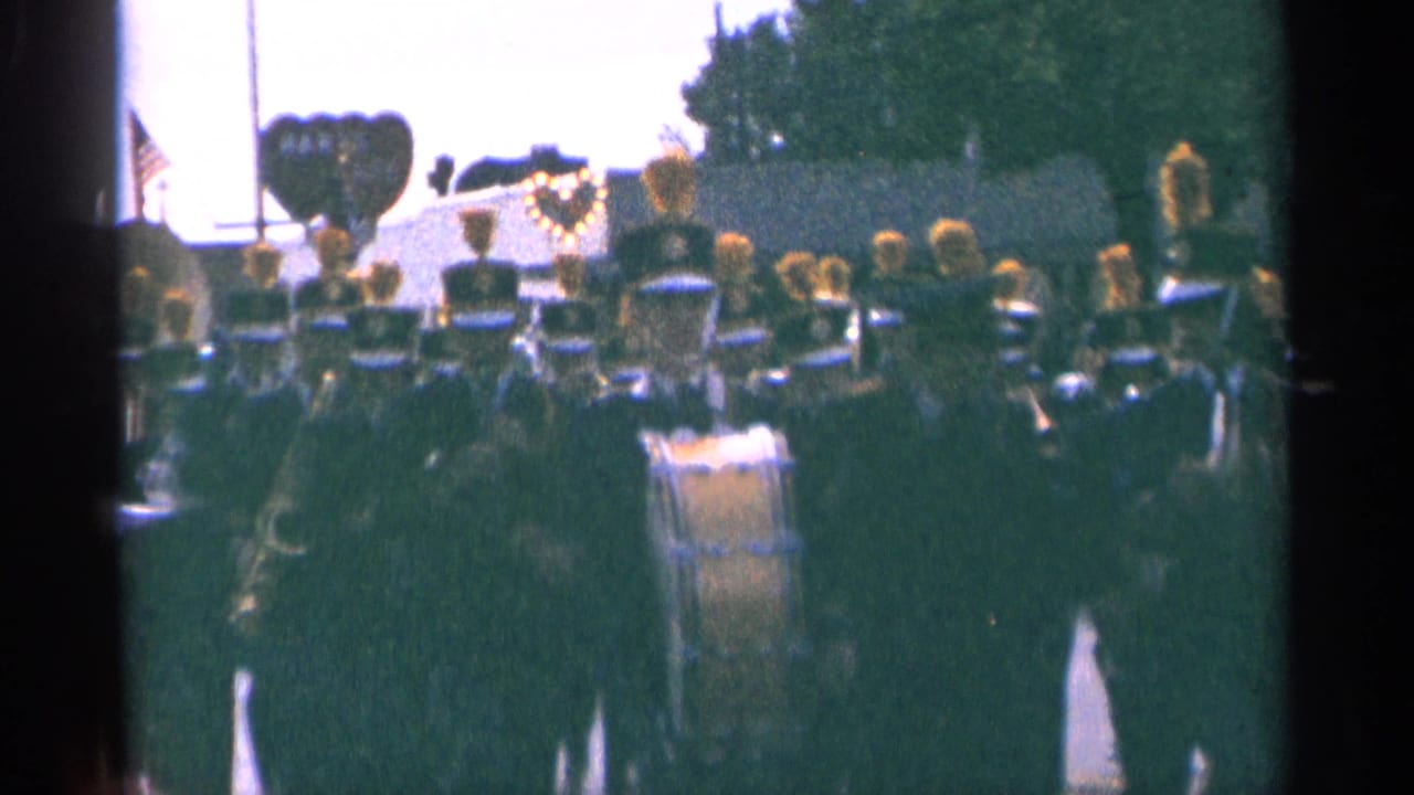 Large marching band in formation during a 1964 Minnesota parade, filmed in soft handheld 8mm color.