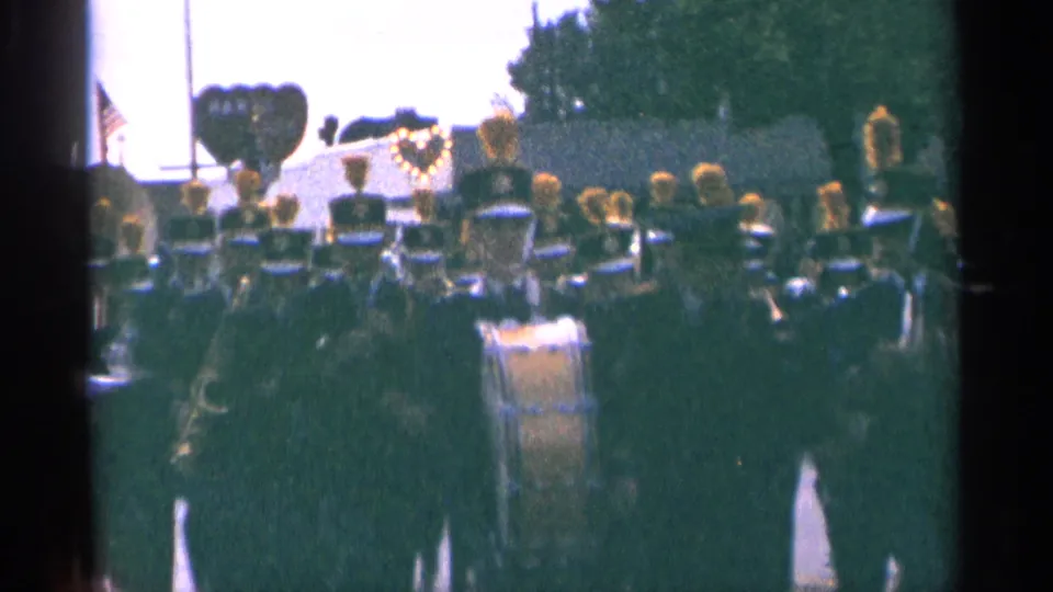 Large marching band in formation during a 1964 Minnesota parade, filmed in soft handheld 8mm color.