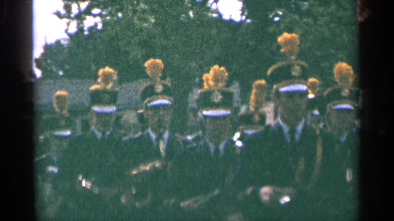 Close 1964 Minnesota home-movie view of a marching band with plumed hats, dark uniforms, and instruments partly visible.