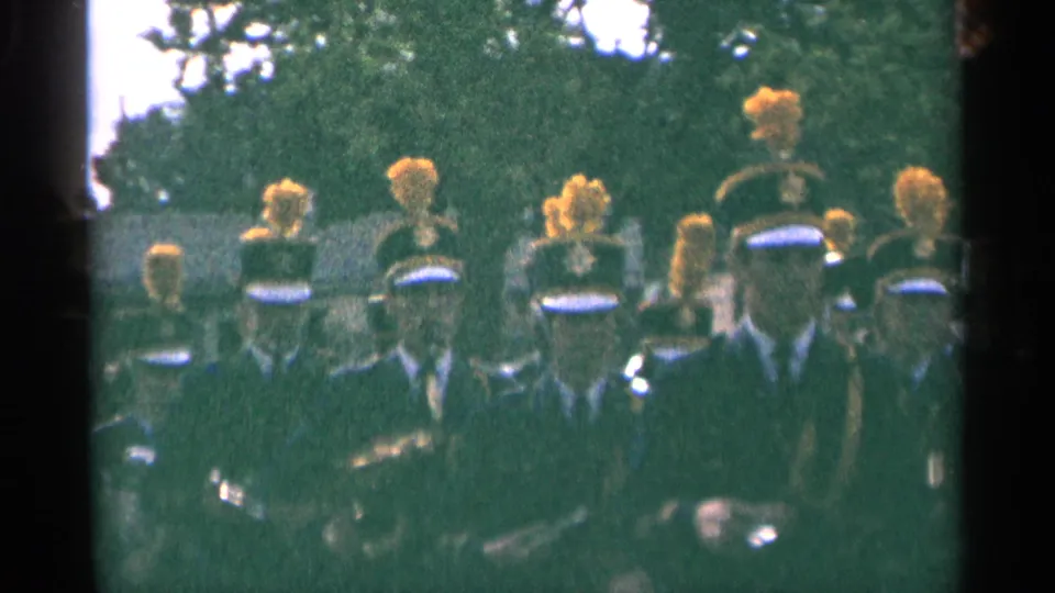 Close 1964 Minnesota home-movie view of a marching band with plumed hats, dark uniforms, and instruments partly visible.