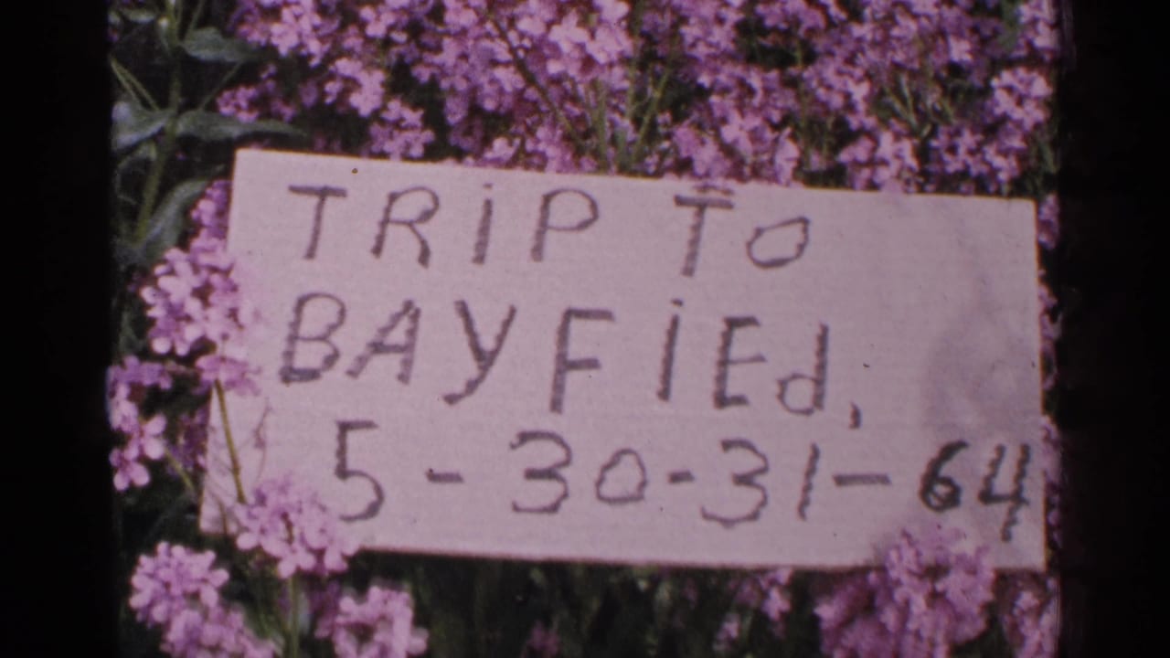 Close view of the hand-lettered Bayfield trip card dated 5-30-31-64, with purple flowers behind it.