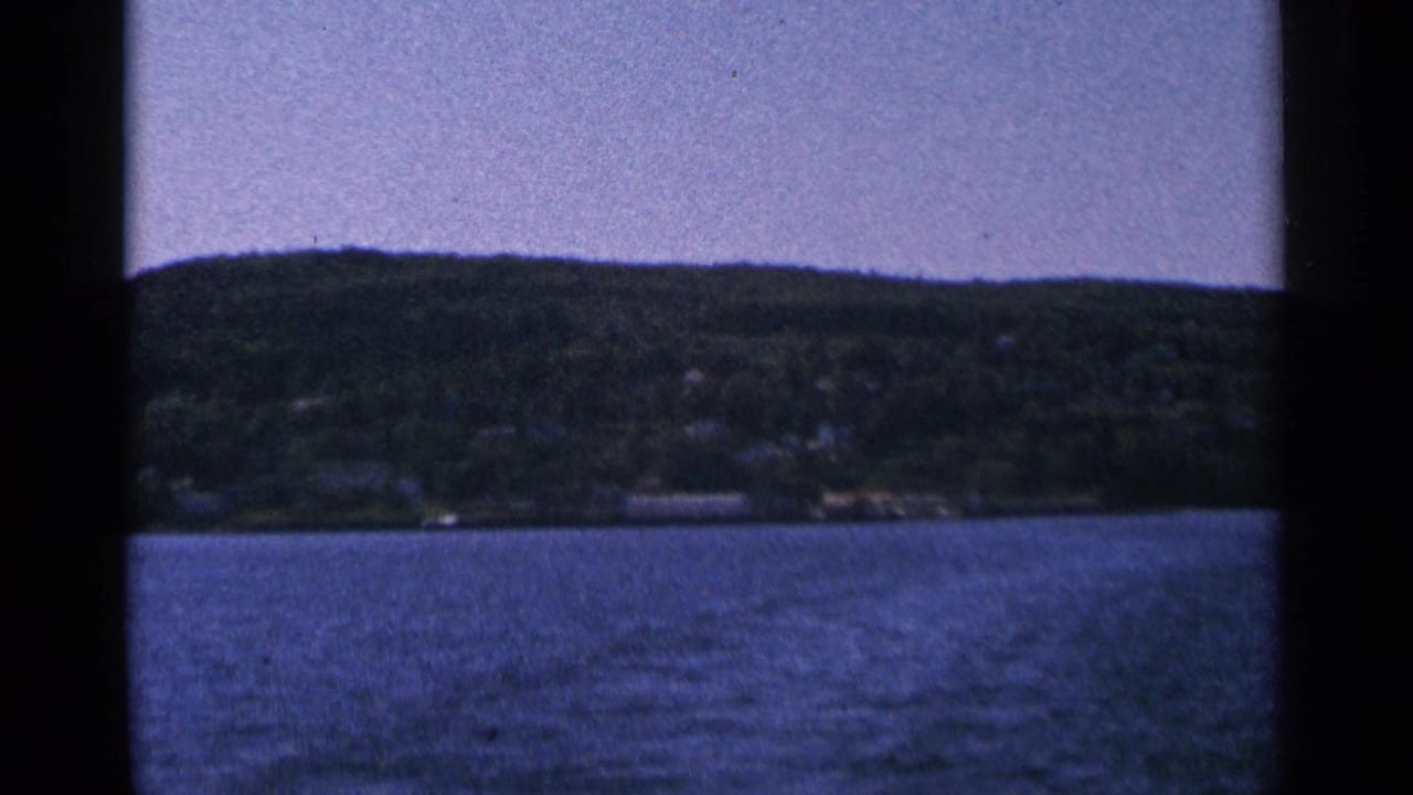 Scenic 8mm view of a tree-covered shoreline across a body of water, likely from the Bayfield trip context.