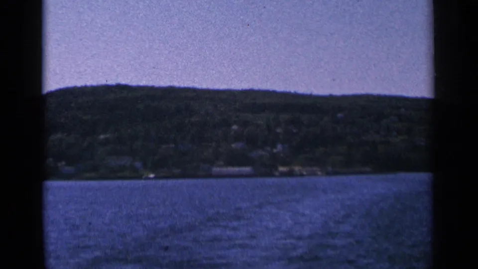 Scenic 8mm view of a tree-covered shoreline across a body of water, likely from the Bayfield trip context.