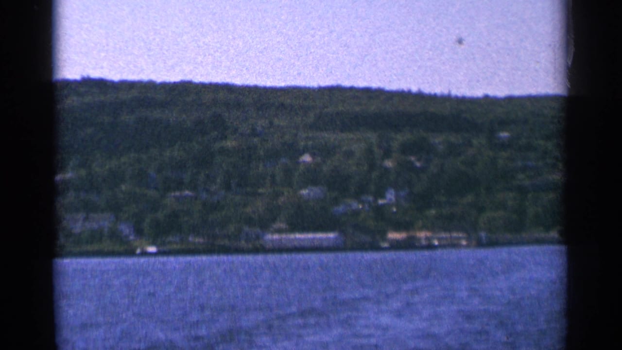 Distant wooded lakeshore with scattered houses above rippled water.