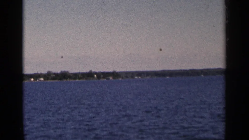 1964 Minnesota home-movie view across open water toward a low distant shoreline.
