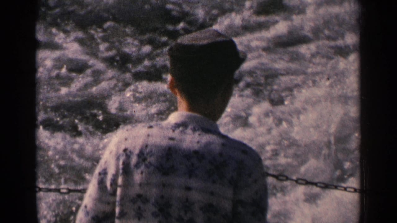 A man in a dark cap and patterned shirt stands at a boat railing as the wake churns behind him in Minnesota, 1964.