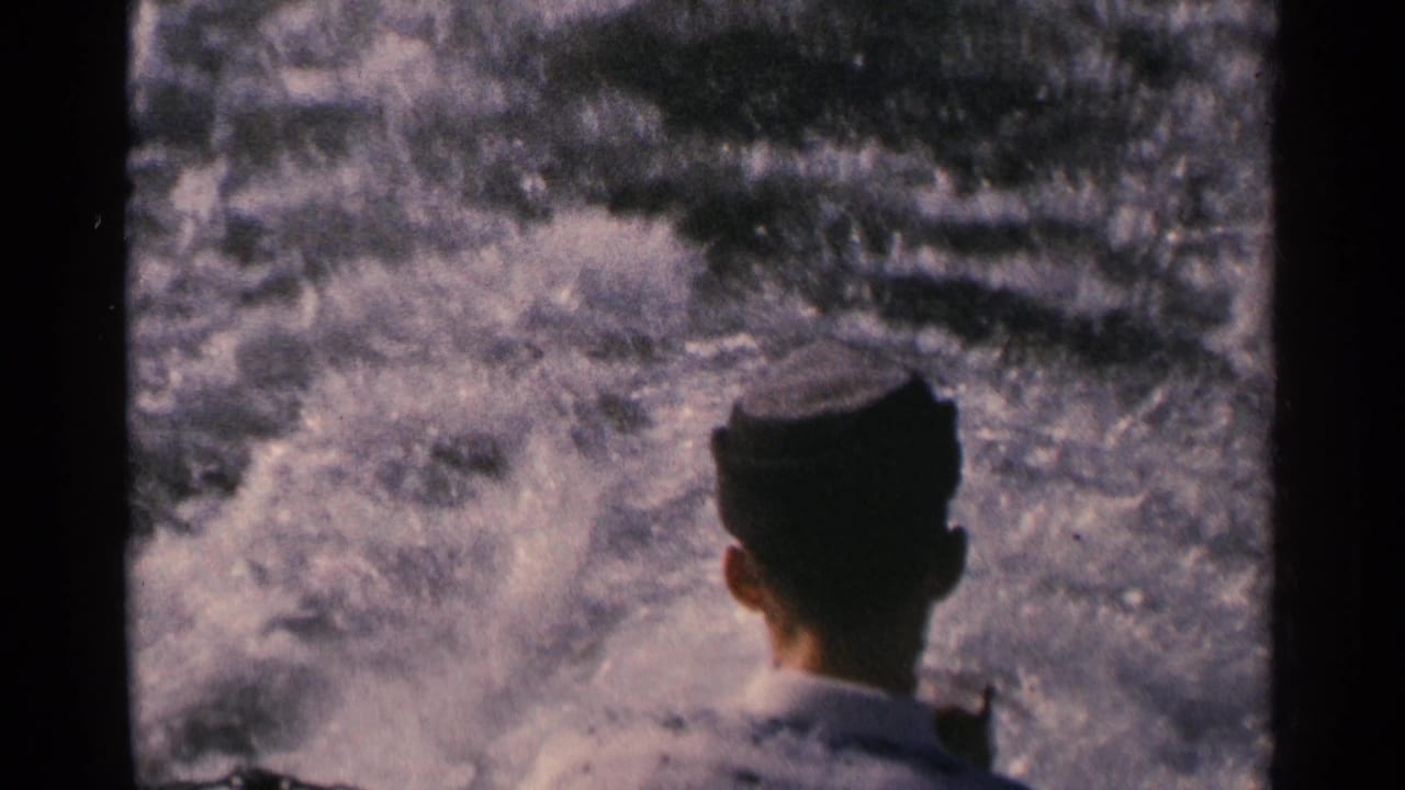 Rear view of a man in a cap watching the boat's turbulent wake in 1964 Minnesota home-movie footage.