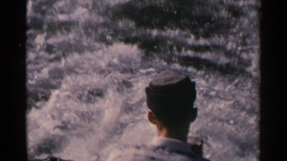 Rear view of a man in a cap watching the boat's turbulent wake in 1964 Minnesota home-movie footage.
