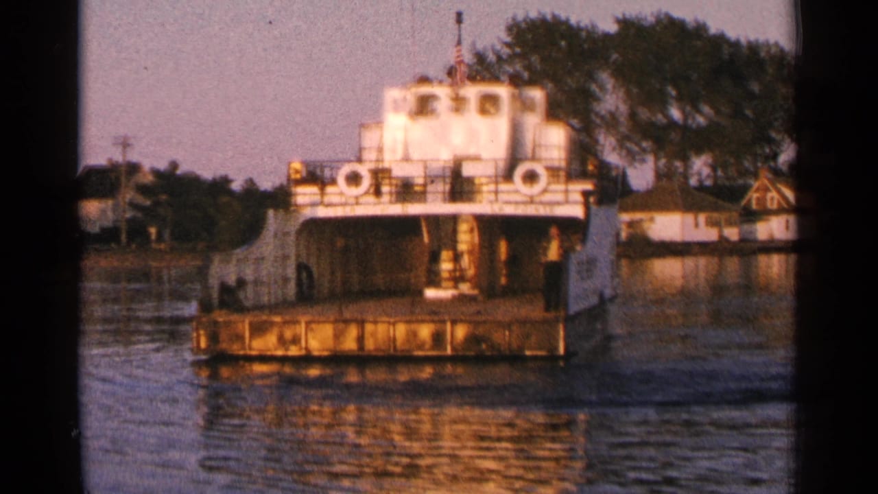 White ferry facing camera on calm lake water near a wooded shoreline.