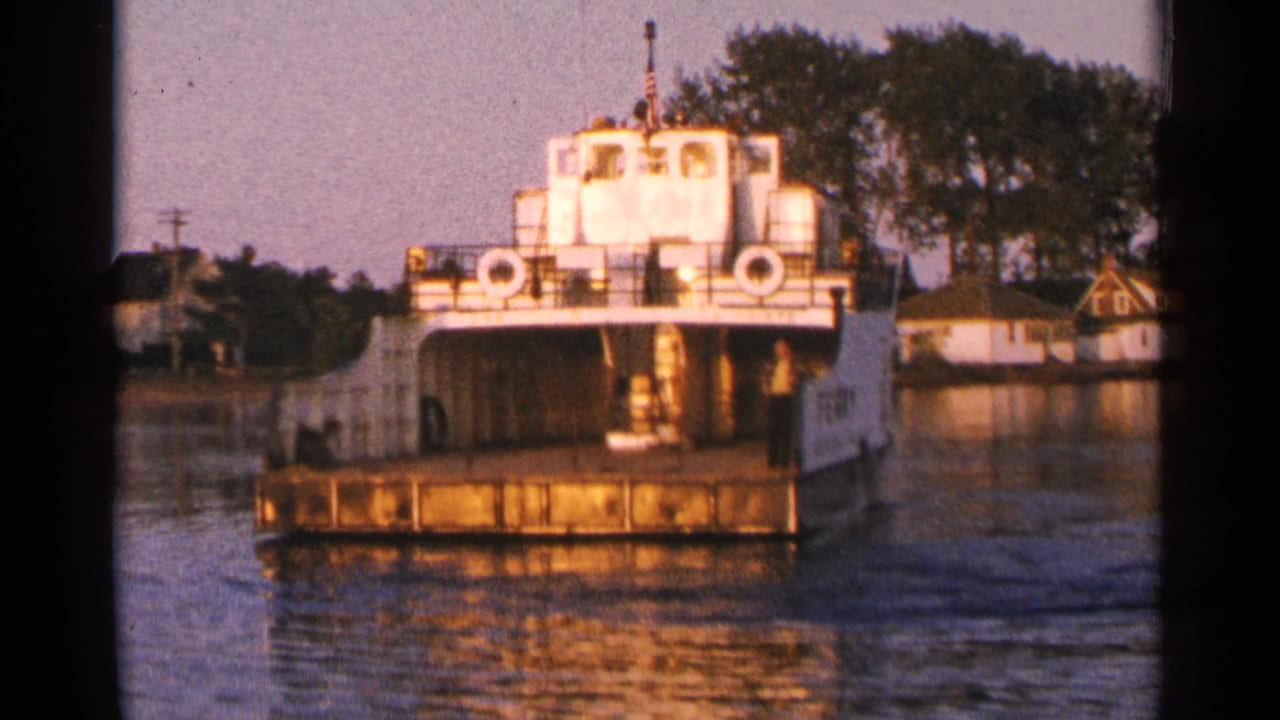The ferry remains centered on the lake, with warm light on its white upper deck and a wooded Minnesota shoreline beyond.