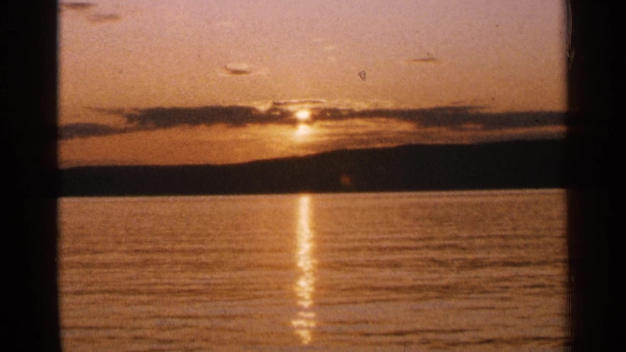 A warm 8mm sunset view over Minnesota lake water shows the sun near a dark shoreline with its reflection stretching toward camera.