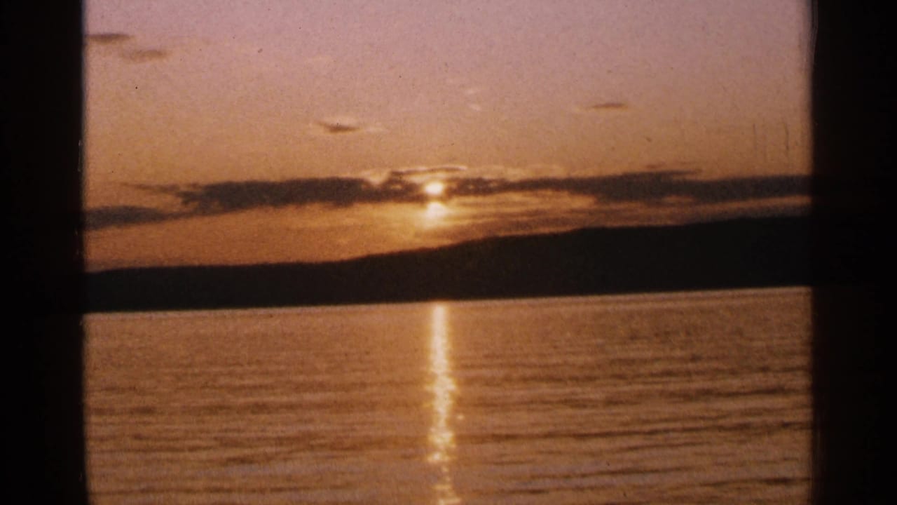Sunset over a calm lake with a golden reflection and dark shoreline.