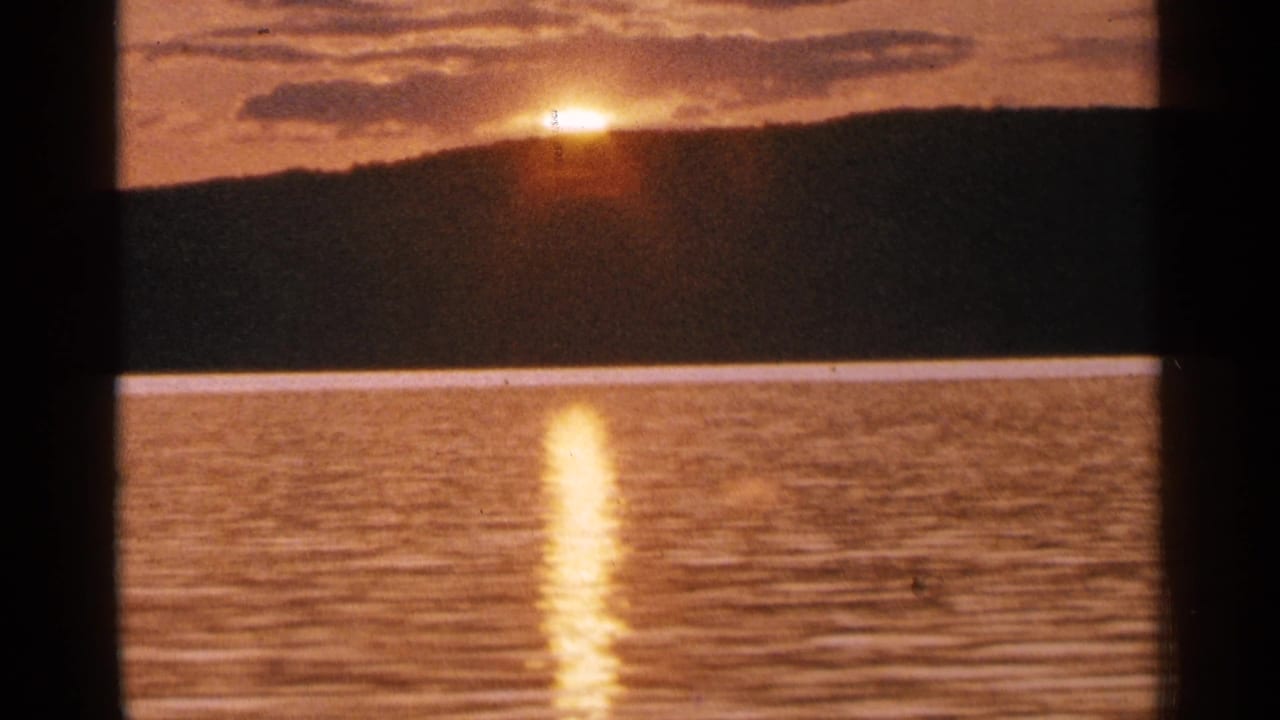 1964 Minnesota 8mm view of a low orange sun, dark lakeside hill, and shimmering reflection on the water below.